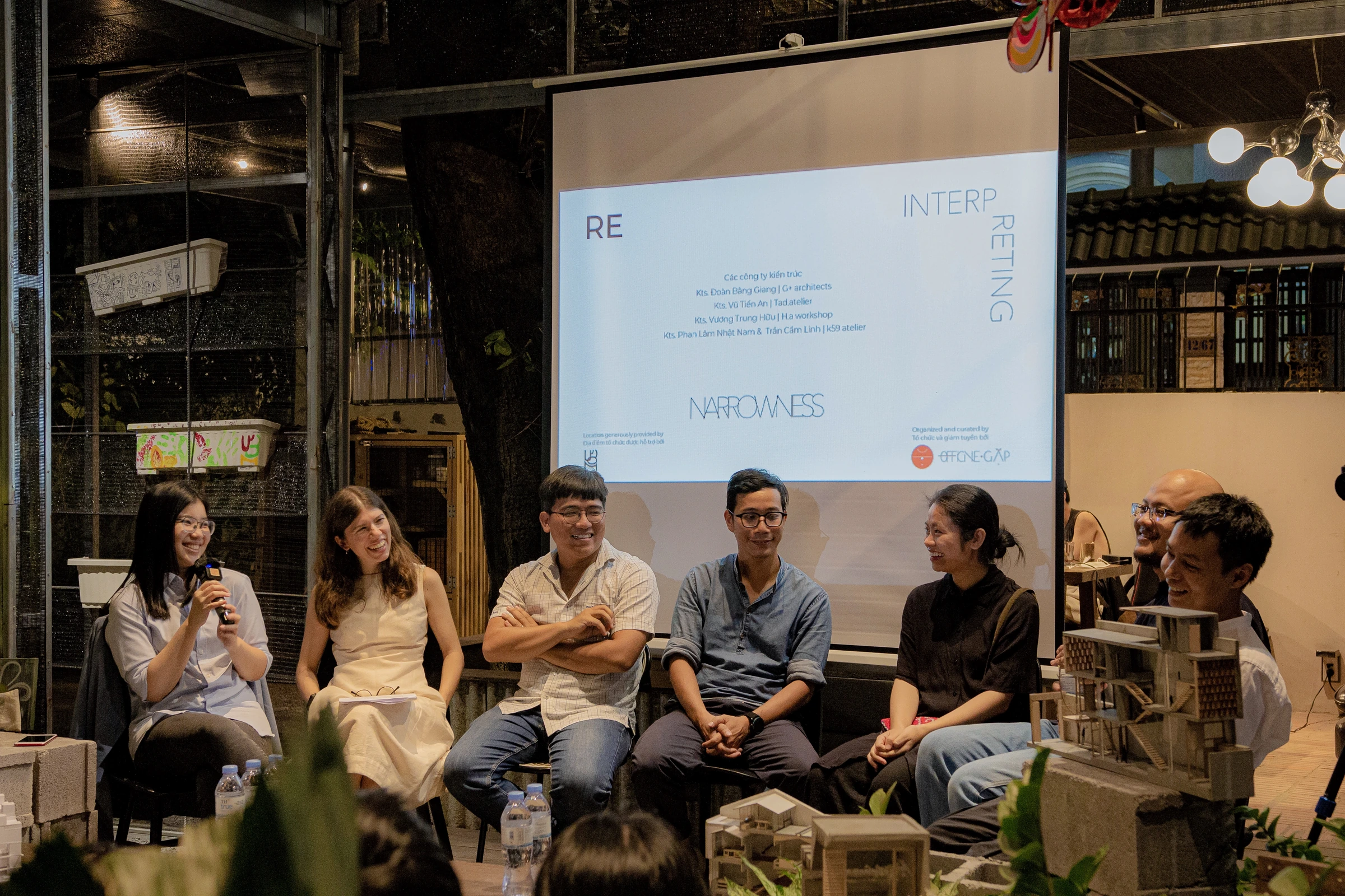 A conversation at Reinterpreting Narrowness, with architectural models and the event projection behind the speakers.