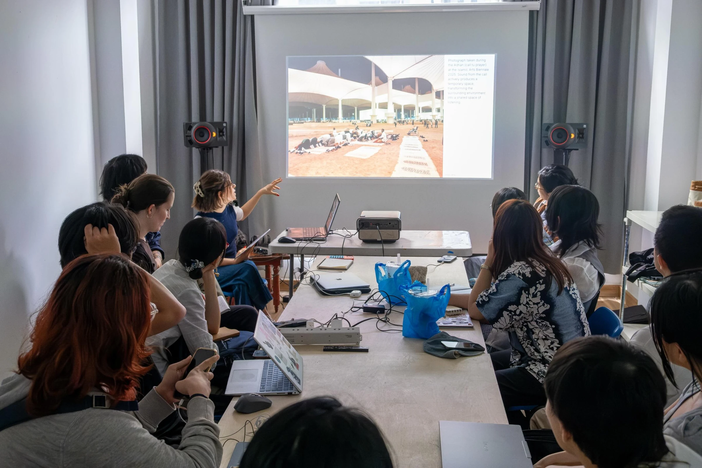 Participants at a table during the Urban Listening workshop at Rare Sea Gallery, with a projected image and speakers at the front of the room.